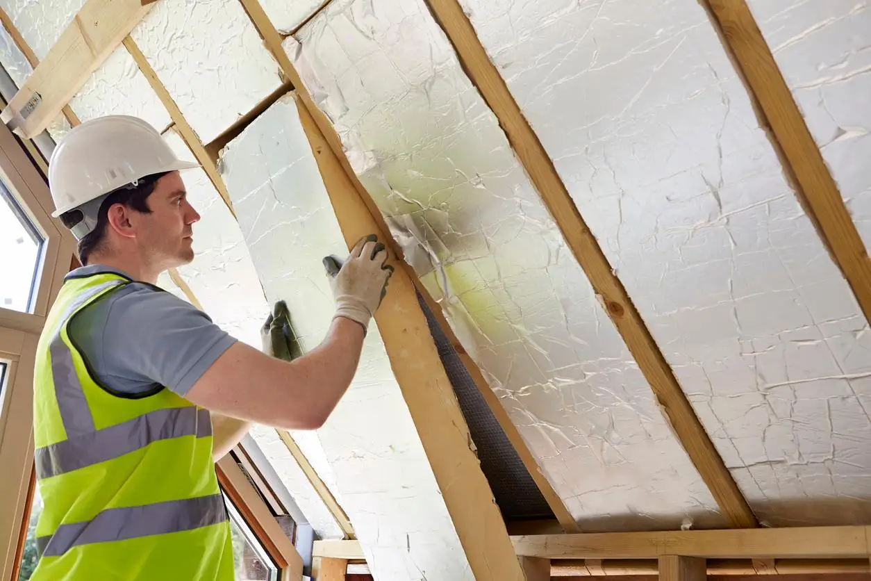 Installer fitting rigid PIR insulation board in loft space